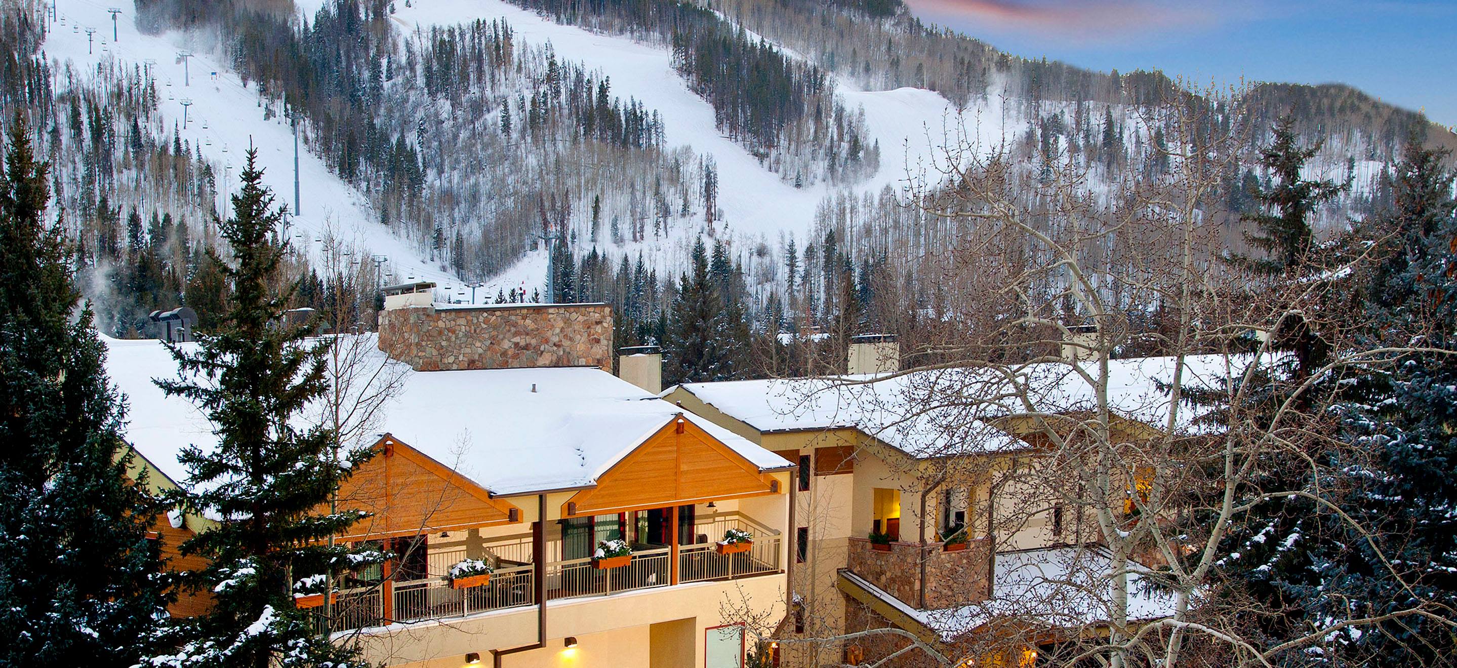 A snowy exterior view of a building with a balcony and chimney, set against a mountainous backdrop.